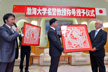 杨校长（中）赠予中国传统工艺“龙”与“凤”的剪纸予池田会长，由创价大学校长山本英夫（左）代表接受