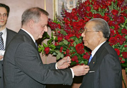 El embajador Bely (izquierda) coloca la insignia de la Orden de la Amistad en la solapa del presidente Ikeda (derecha)
