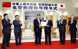 Presidente Asihaer Tuersun coloca el objeto distintivo en manos de Hideo Yamamoto, presidente de la Universidad Soka, en sustitución de Daisaku Ikeda