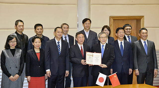 Shang (cuarto desde la izquierda en la primera fila) hace entrega del certificado de nombramiento al presidente de la Universidad Soka, Baba (tercero desde la derecha en la primera fila)