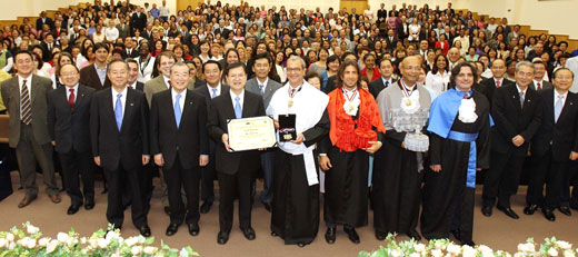 El rector Marcos Antonio Gagliardi Cascino (primer plano, cuarto desde la derecha) entrega los símbolos honorarios a Hiromasa Ikeda, hijo del destinatario, Daisaku Ikeda (primer plano, tercero desde la izquierda)